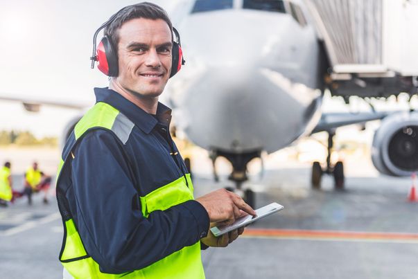 Porträt eines lächelnden Arbeiters, der am Flughafen stehend Informationen in ein digitales Gerät schreibt